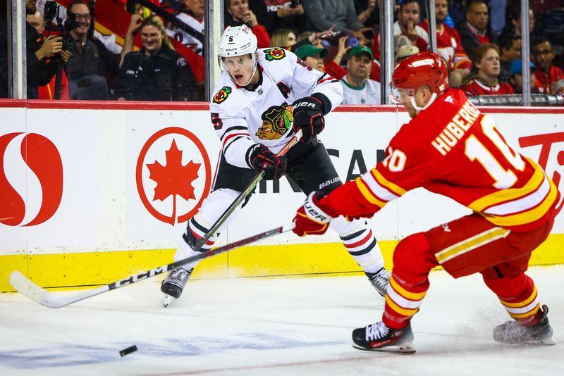 Oct 15, 2024; Calgary, Alberta, CAN; Chicago Blackhawks defenseman Connor Murphy (5) passes the puck against Calgary Flames center Jonathan Huberdeau (10) during the second period at Scotiabank Saddledome. Mandatory Credit: Sergei Belski-Imagn Images