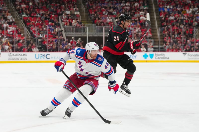 Nov 26, 2025; Raleigh, North Carolina, USA; Carolina Hurricanes center Seth Jarvis (24) jumps by the check of New York Rangers defenseman Vladislav Gavrikov (44) during the third period at Lenovo Center. Mandatory Credit: James Guillory-Imagn Images