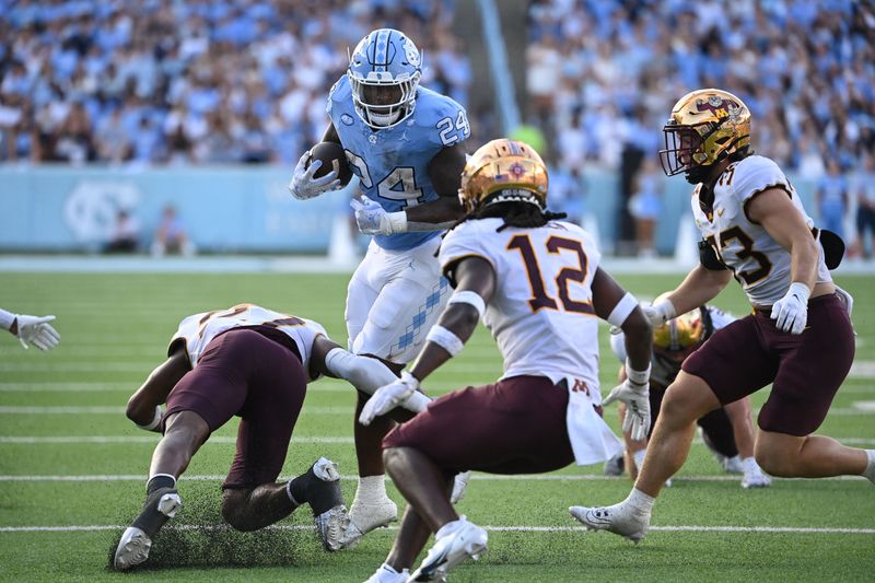 Sep 16, 2023; Chapel Hill, North Carolina, USA; North Carolina Tar Heels running back British Brooks (24) with the ball as Minnesota Golden Gophers defensives back Tyler Nubin (27) and Darius Green (12) and linebacker Ryan Selig (33) defend in the fourth quarter at Kenan Memorial Stadium. Mandatory Credit: Bob Donnan-USA TODAY Sports