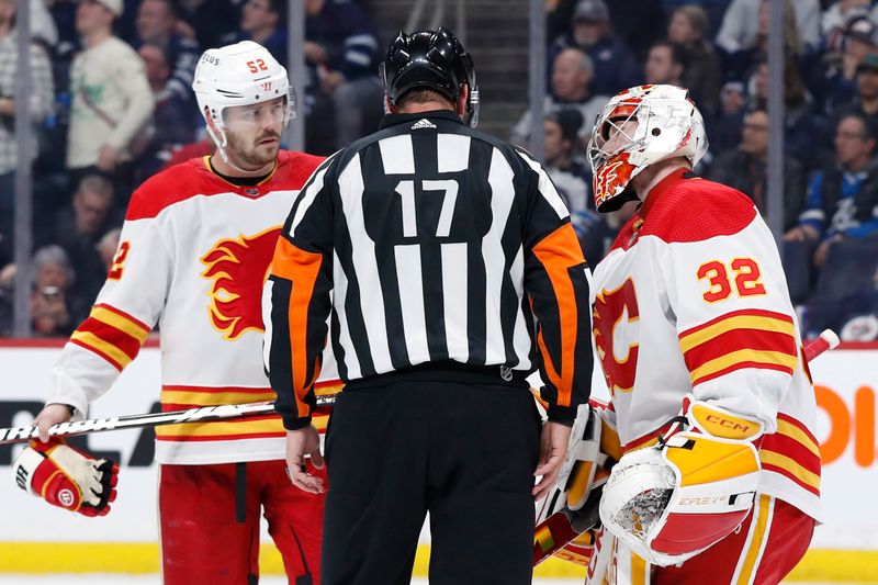 Apr 4, 2024; Winnipeg, Manitoba, CAN; Calgary Flames defenseman MacKenzie Weegar (52) and Calgary Flames goaltender Dustin Wolf (32) talk with referee Frederick L'Ecuyer (17) during a break in the play in the second period against the Winnipeg Jets at Canada Life Centre. Mandatory Credit: James Carey Lauder-USA TODAY Sports