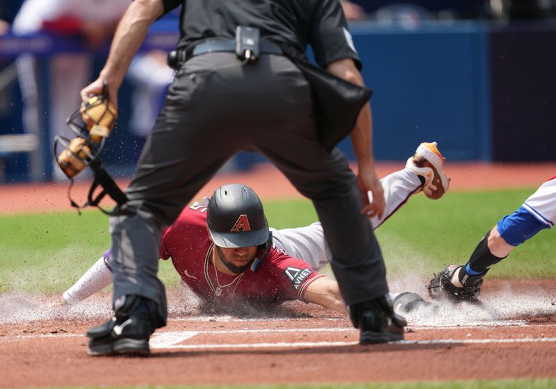 Jul 16, 2023; Toronto, Ontario, CAN; Arizona Diamondbacks left fielder Lourdes Gurriel Jr. (12) slides into home scoring a run against the Toronto Blue Jays during the first inning at Rogers Centre. Mandatory Credit: Nick Turchiaro-USA TODAY Sports