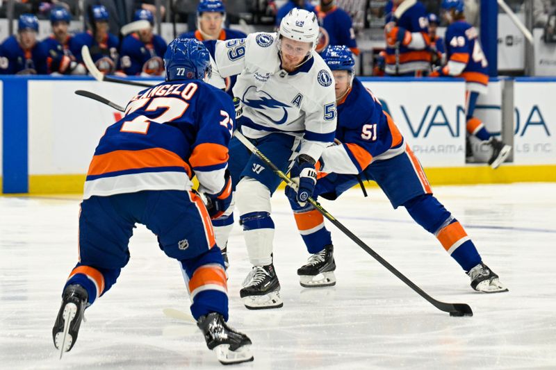 Dec 13, 2025; Elmont, New York, USA; Tampa Bay Lightning center Jake Guentzel (59) attempts a shit defended by New York Islanders defenseman Tony Deangelo (77) during the first period at UBS Arena. Mandatory Credit: Dennis Schneidler-Imagn Images