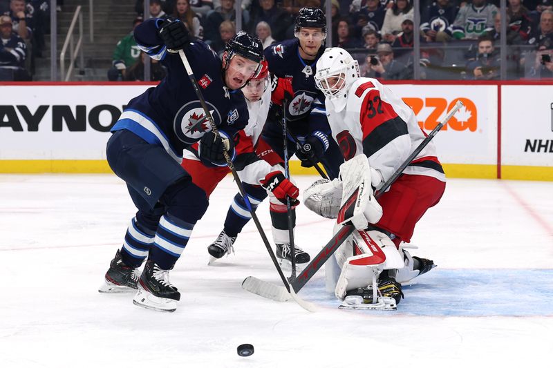 Nov 21, 2025; Winnipeg, Manitoba, CAN; Winnipeg Jets center Jonathan Toews (19) and Carolina Hurricanes goaltender Brandon Bussi (32) eye the puck during the second period at Canada Life Centre. Mandatory Credit: James Carey Lauder-Imagn Images