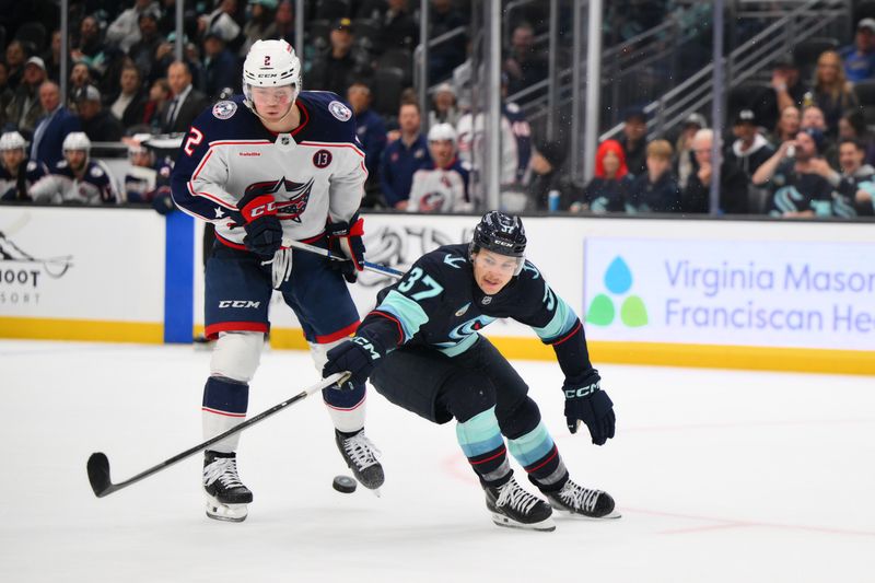 Nov 12, 2024; Seattle, Washington, USA; Seattle Kraken center Yanni Gourde (37) reaches for the puck while defended by Columbus Blue Jackets defenseman Jake Christiansen (2) during the third period at Climate Pledge Arena. Mandatory Credit: Steven Bisig-Imagn Images