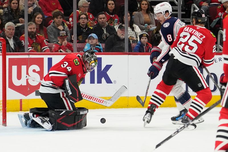 Dec 1, 2024; Chicago, Illinois, USA; Chicago Blackhawks goaltender Petr Mrazek (34) makes a save on Columbus Blue Jackets defenseman Zach Werenski (8) during the second period at United Center. Mandatory Credit: David Banks-Imagn Images