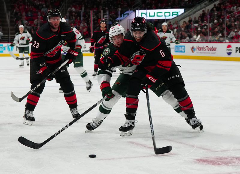 Jan 21, 2024; Raleigh, North Carolina, USA;  Carolina Hurricanes defenseman Jalen Chatfield (5) and Minnesota Wild center Jacob Lucchini (27) battle over the puck during the second period at PNC Arena. Mandatory Credit: James Guillory-USA TODAY Sports