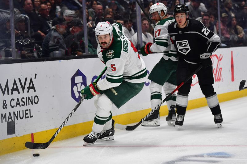 Mar 20, 2024; Los Angeles, California, USA; Minnesota Wild defenseman Jake Middleton (5) moves the puck ahead of Los Angeles Kings defenseman Jordan Spence (21) during the third period at Crypto.com Arena. Mandatory Credit: Gary A. Vasquez-USA TODAY Sports