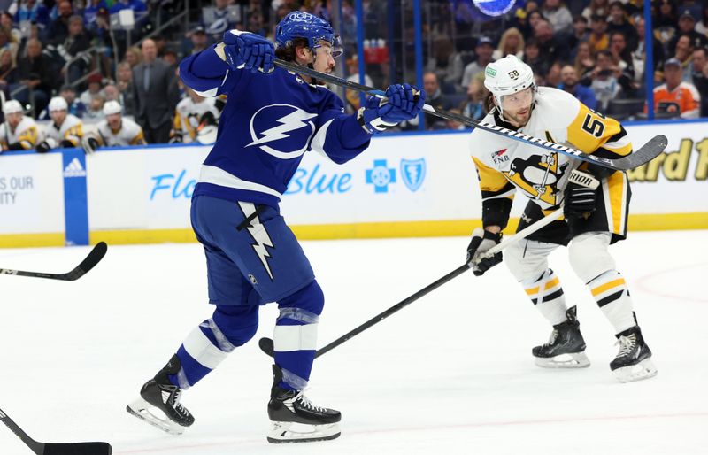 Dec 6, 2023; Tampa, Florida, USA; Tampa Bay Lightning center Alex Barre-Boulet (12) shoots as Pittsburgh Penguins defenseman Kris Letang (58) defends during the first period at Amalie Arena. Mandatory Credit: Kim Klement Neitzel-USA TODAY Sports