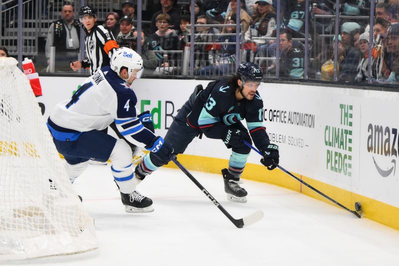 Mar 8, 2024; Seattle, Washington, USA; Seattle Kraken left wing Brandon Tanev (13) plays the puck against the wall while defended by Winnipeg Jets defenseman Neal Pionk (4) during the second period at Climate Pledge Arena. Mandatory Credit: Steven Bisig-USA TODAY Sports