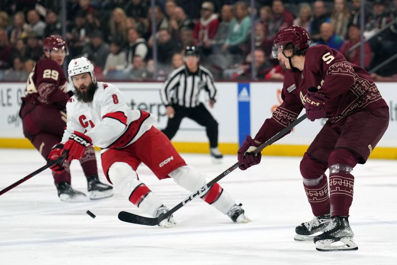 Mar 3, 2023; Tempe, Arizona, USA; Arizona Coyotes defenseman Michael Kesselring (5) passes the puck by Carolina Hurricanes defenseman Brent Burns (8) during the first period at Mullett Arena. Mandatory Credit: Joe Camporeale-USA TODAY Sports