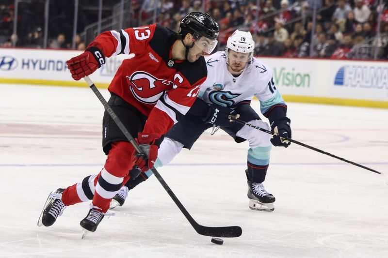 Dec 6, 2024; Newark, New Jersey, USA; New Jersey Devils center Nico Hischier (13) skates with the puck while being defended by Seattle Kraken left wing Jared McCann (19) during the second period at Prudential Center. Mandatory Credit: Ed Mulholland-Imagn Images