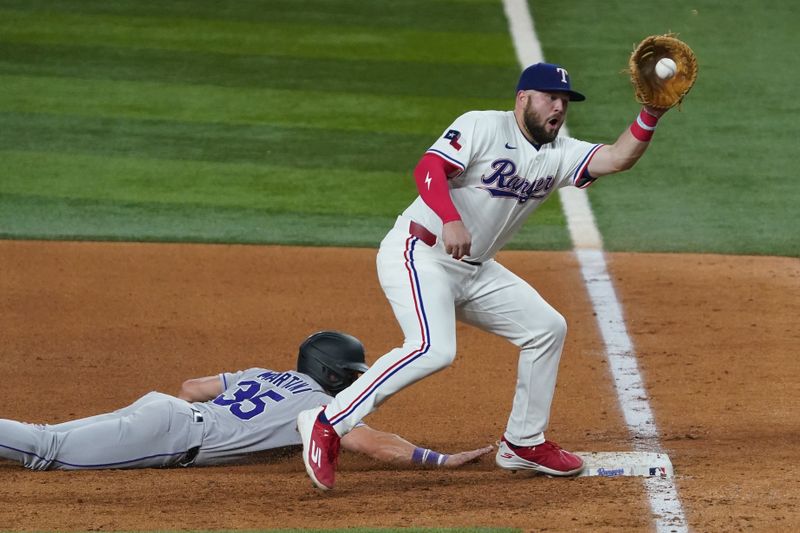 May 13, 2025; Arlington, Texas, USA; Texas Rangers first baseman Jake Burger (21) prepares to apply the tag on a pickoff attempt as Colorado Rockies outfielder Nick Martini (35) slide back safely during the fifth inning at Globe Life Field. Mandatory Credit: Raymond Carlin III-Imagn Images