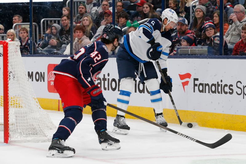 Mar 17, 2024; Columbus, Ohio, USA; Winnipeg Jets defenseman Brenden Dillon (5) passes the puck as Columbus Blue Jackets center Alexander Texier (42) trails the play during the second period at Nationwide Arena. Mandatory Credit: Russell LaBounty-USA TODAY Sports