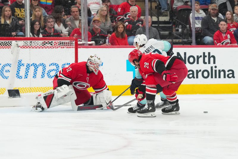 Jan 10, 2026; Raleigh, North Carolina, USA;  Seattle Kraken left wing Tye Kartye (12) loses control of the puck against left wing William Carrier (28) and Carolina Hurricanes goaltender Brandon Bussi (32) during the first period at Lenovo Center. Mandatory Credit: James Guillory-Imagn Images