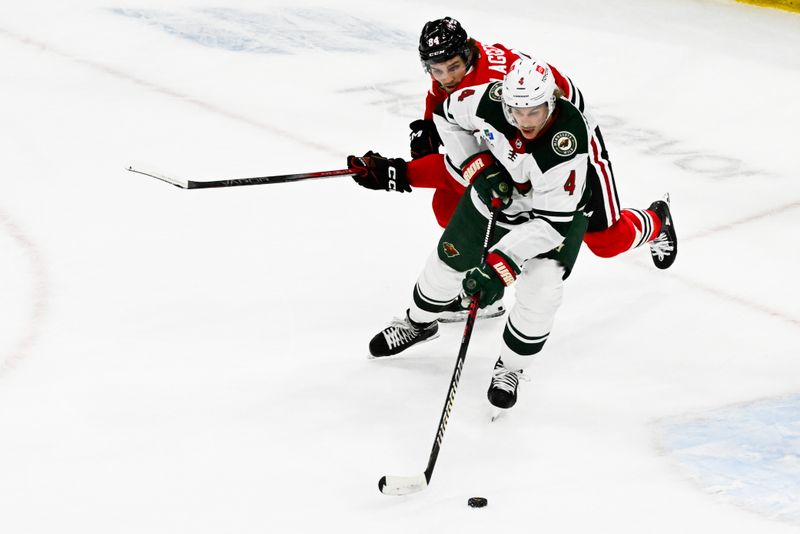 Apr 7, 2024; Chicago, Illinois, USA;  Chicago Blackhawks left wing Landon Slaggert (84) and Minnesota Wild defenseman Jon Merrill (4) chase the puck during the second period at United Center. Mandatory Credit: Matt Marton-USA TODAY Sports