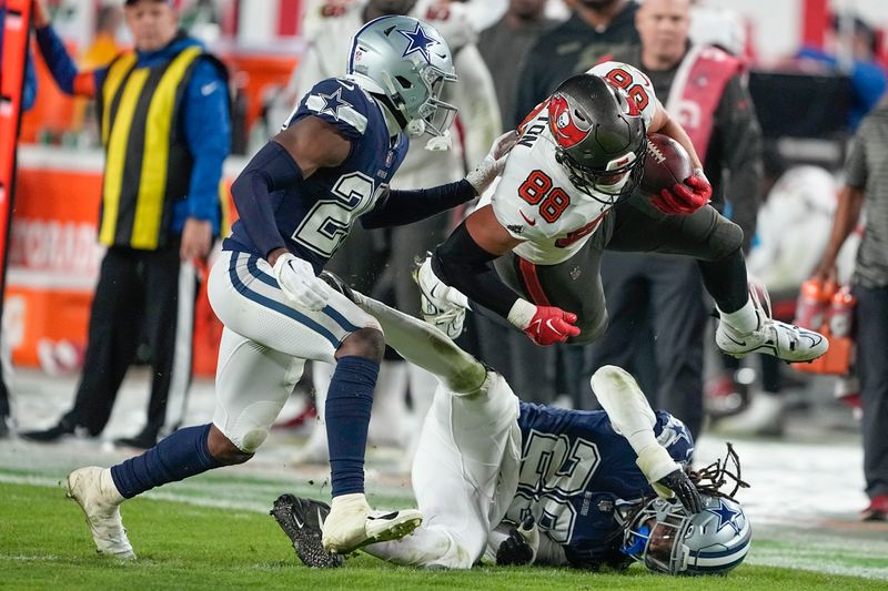 Tampa Bay Buccaneers tight end Cade Otton (88) jumps over Dallas Cowboys safety Malik Hooker (28) during the second half of an NFL wild-card football game, Monday, Jan. 16, 2023, in Tampa, Fla. (AP Photo/Chris Carlson)