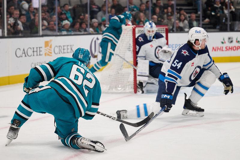 Dec 12, 2023; San Jose, California, USA; San Jose Sharks right wing Kevin Labanc (62) shoots the puck against Winnipeg Jets defenseman Dylan Samberg (54) and goaltender Laurent Brossoit (39) during the second period at SAP Center at San Jose. Mandatory Credit: Robert Edwards-USA TODAY Sports