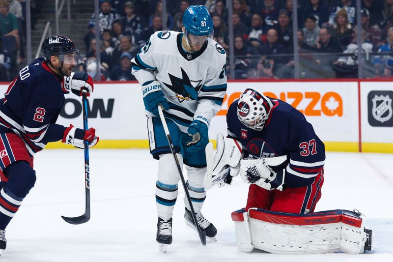 Oct 18, 2024; Winnipeg, Manitoba, CAN;  Winnipeg Jets goalie Connor Hellebuyck (37) makes a save as San Jose Sharks forward Alexander Wennberg (21) looks for a rebound during the first period at Canada Life Centre. Mandatory Credit: Terrence Lee-Imagn Images