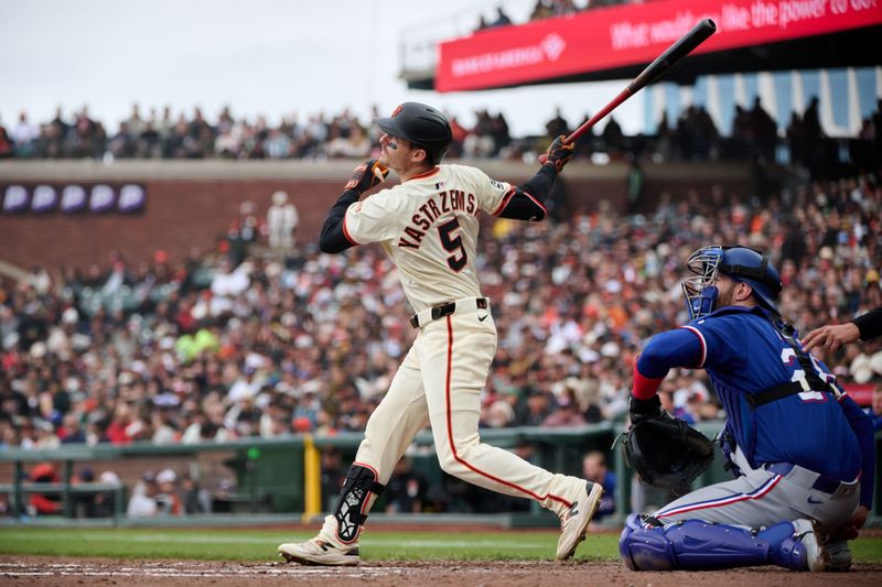 Apr 27, 2025; San Francisco, California, USA; San Francisco Giants outfielder Mike Yastrzemski (5) hits a single against Texas Rangers catcher Jonah Heim (28) during the seventh inning at Oracle Park. Mandatory Credit: Robert Edwards-Imagn Images