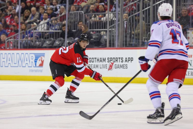 Apr 5, 2025; Newark, New Jersey, USA; New Jersey Devils center Cody Glass (12) skates with the puck as New York Rangers defenseman Will Borgen (17) defends during the second period at Prudential Center. Mandatory Credit: Ed Mulholland-Imagn Images