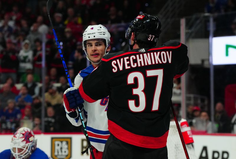 Mar 12, 2024; Raleigh, North Carolina, USA; New York Rangers defenseman Braden Schneider (4) and Carolina Hurricanes right wing Andrei Svechnikov (37) battle in the third period at PNC Arena. Mandatory Credit: James Guillory-USA TODAY Sports