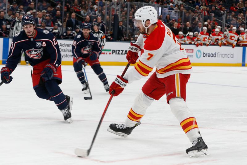 Jan 13, 2026; Columbus, Ohio, USA; Calgary Flames defenseman Kevin Bahl (7) wrists a shot on goal against as Columbus Blue Jackets center Sean Monahan (23) trails the play during the first period at Nationwide Arena. Mandatory Credit: Russell LaBounty-Imagn Images