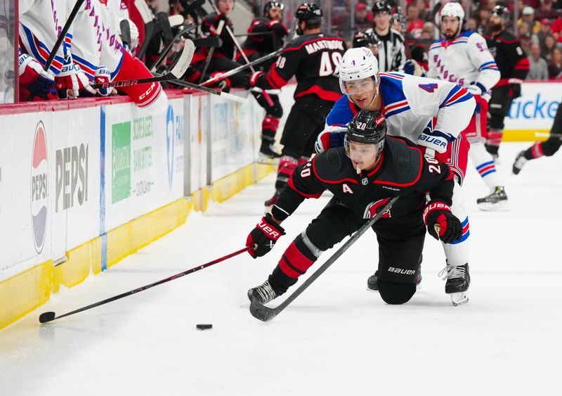 Apr 12, 2025; Raleigh, North Carolina, USA;  New York Rangers defenseman Braden Schneider (4) checks Carolina Hurricanes center Sebastian Aho (20) during the first period at Lenovo Center. Mandatory Credit: James Guillory-Imagn Images
