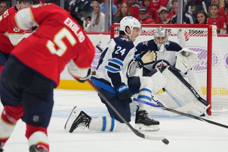 Nov 16, 2024; Sunrise, Florida, USA;  Winnipeg Jets goaltender Connor Hellebuyck (37) prepares to make a save  and defenseman Haydn Fleury (24) moves in to block as Florida Panthers defenseman Aaron Ekblad (5) takes a shot during the second period at Amerant Bank Arena. Mandatory Credit: Jim Rassol-Imagn Images