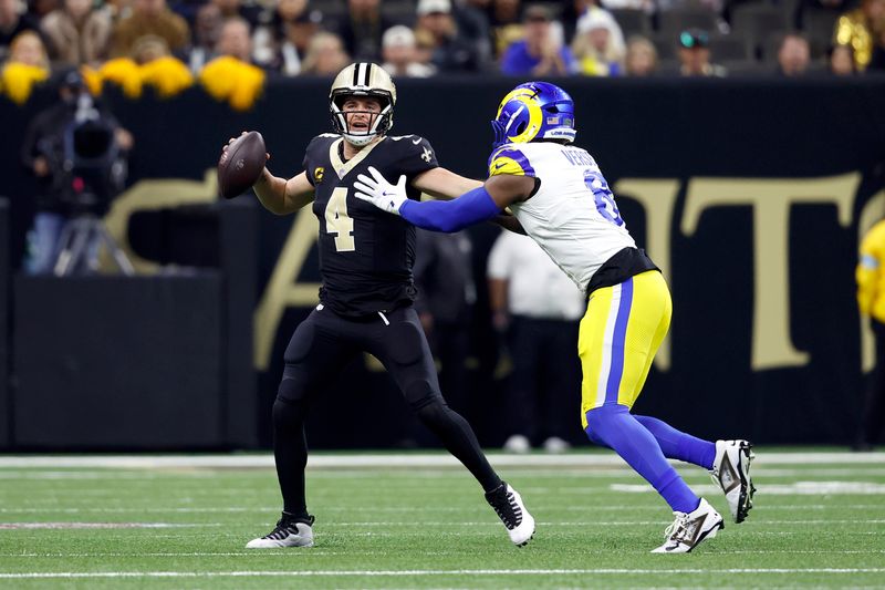 New Orleans Saints quarterback Derek Carr (4) is defended by Los Angeles Rams linebacker Jared Verse (8) Los Angeles Rams cornerback Tre Tomlinson (6) during an NFL football game, Sunday, Dec. 1, 2024, in New Orleans. (AP Photo/Tyler Kaufman)