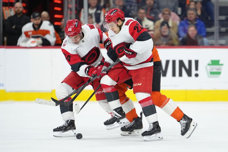 Dec 13, 2025; Philadelphia, Pennsylvania, USA; Carolina Hurricanes defenseman Joel Nystrom (64) and center Logan Stankoven (22) battle for the puck against Philadelphia Flyers left wing Noah Cates (27) in the second period at Xfinity Mobile Arena. Mandatory Credit: Kyle Ross-Imagn Images