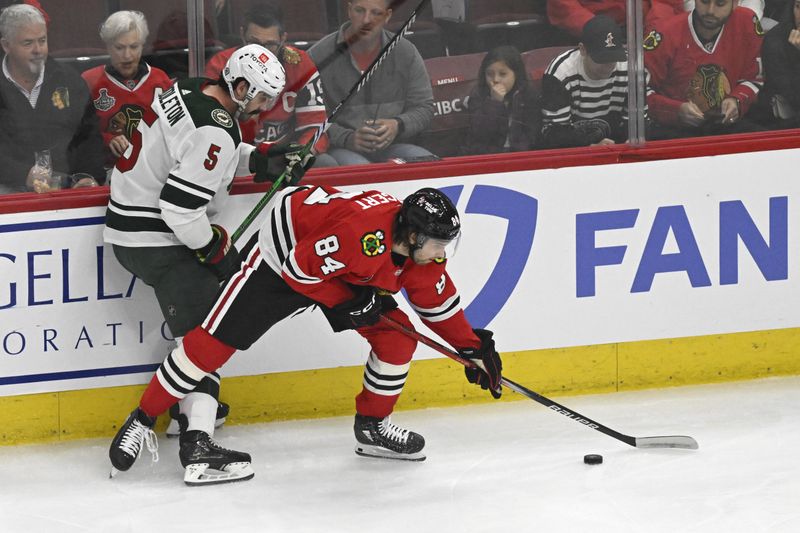 Apr 7, 2024; Chicago, Illinois, USA;  Chicago Blackhawks left wing Landon Slaggert (84) and Minnesota Wild defenseman Jake Middleton (5) chase the puck during the first period at the United Center. Mandatory Credit: Matt Marton-USA TODAY Sports