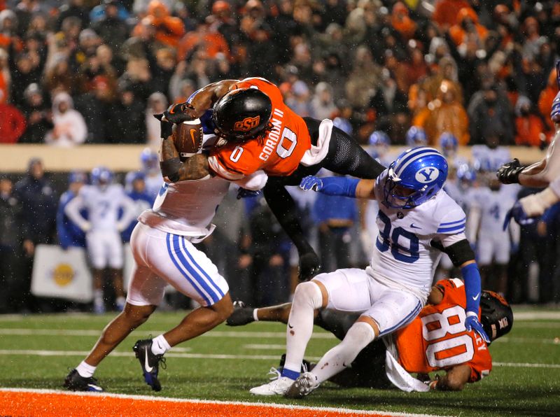 Nov 25, 2023; Stillwater, Oklahoma, USA;  Oklahoma State's Ollie Gordon II (0) scores a touchdown in the second overtime against BYU's Eddie Heckard (5) and Crew Wakley (38) at Boone Pickens Stadium. Mandatory Credit: Sarah Phipps-USA TODAY Sports