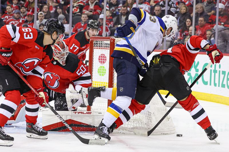 Mar 7, 2024; Newark, New Jersey, USA; St. Louis Blues left wing Jake Neighbours (63) battles for the puck against New Jersey Devils defenseman Jonas Siegenthaler (71) behind goaltender Nico Daws (50) during the second period at Prudential Center. Mandatory Credit: Vincent Carchietta-USA TODAY Sports