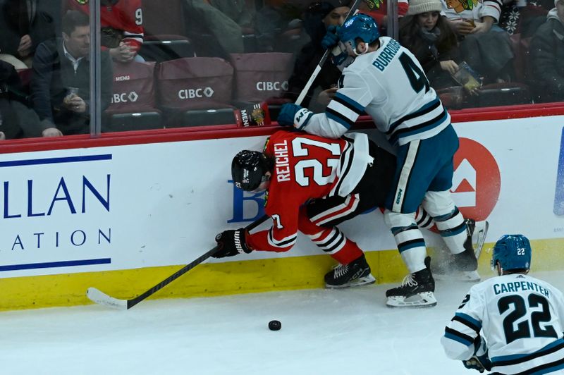 Jan 16, 2024; Chicago, Illinois, USA; Chicago Blackhawks left wing Lukas Reichel (27) and San Jose Sharks defenseman Kyle Burroughs (4) chase the puck during the second period at United Center. Mandatory Credit: Matt Marton-USA TODAY Sports