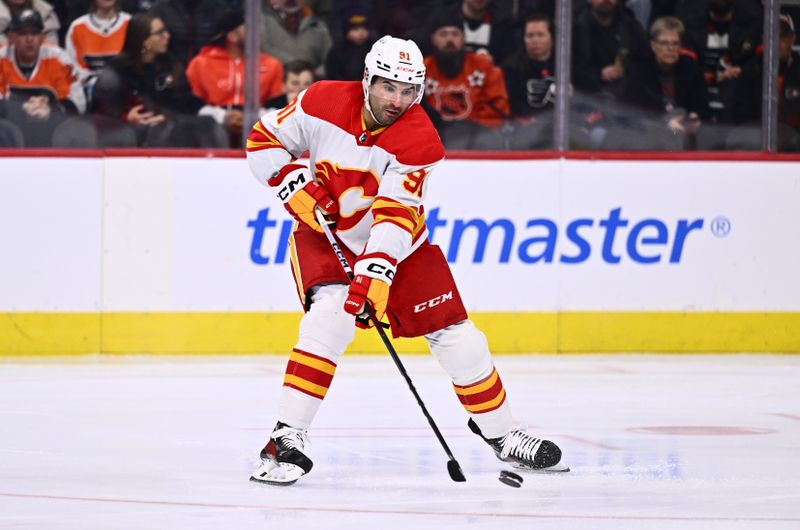 Jan 6, 2024; Philadelphia, Pennsylvania, USA; Calgary Flames center Nazem Kadri (91) reaches for the puck against the Philadelphia Flyers in the first period at Wells Fargo Center. Mandatory Credit: Kyle Ross-USA TODAY Sports