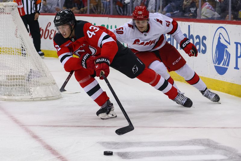 Nov 21, 2024; Newark, New Jersey, USA; New Jersey Devils defenseman Luke Hughes (43) skates with the puck while being defended by Carolina Hurricanes left wing Eric Robinson (50) during the third period at Prudential Center. Mandatory Credit: Ed Mulholland-Imagn Images