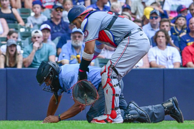 Jul 14, 2024; Milwaukee, Wisconsin, USA; Washington Nationals catcher Keibert Ruiz (20) helps home plate umpire CB Bucknor after he was hit by a foul ball in the third inning against the Milwaukee Brewers at American Family Field. Mandatory Credit: Benny Sieu-USA TODAY Sports