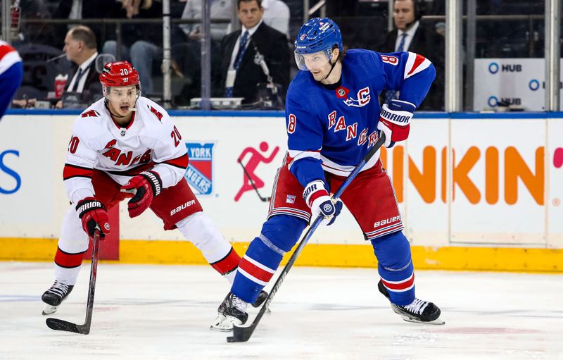 Jan 2, 2024; New York, New York, USA; New York Rangers defenseman Jacob Trouba (8) flips the puck past Carolina Hurricanes left wing Sebastian Aho (20) during the second period at Madison Square Garden. Mandatory Credit: Danny Wild-USA TODAY Sports