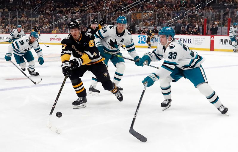 Mar 14, 2024; Pittsburgh, Pennsylvania, USA; Pittsburgh Penguins right wing Rickard Rakell (67) carries the puck into the offensive zone as San Jose Sharks center Mikael Granlund (64) and defenseman Calen Addison (33) defend during the first period at PPG Paints Arena. Mandatory Credit: Charles LeClaire-USA TODAY Sports