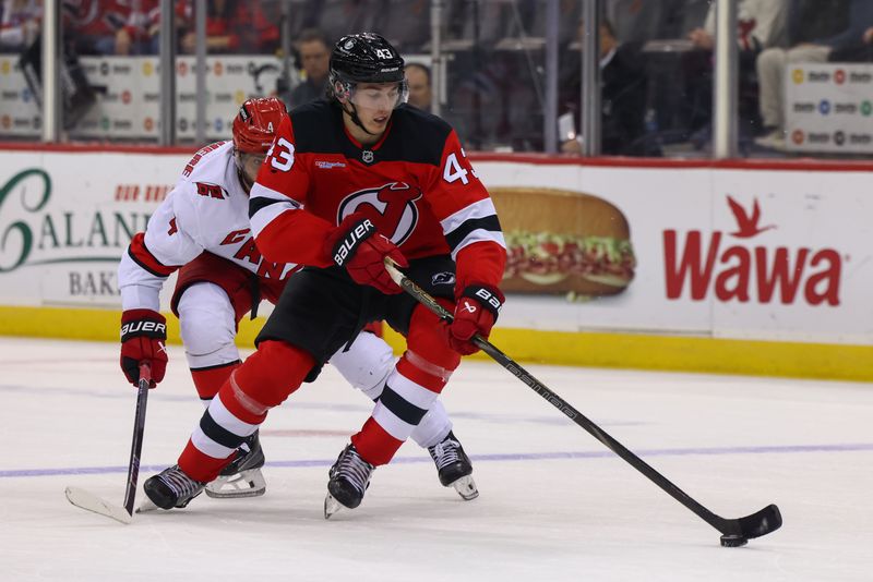 Nov 21, 2024; Newark, New Jersey, USA; New Jersey Devils defenseman Luke Hughes (43) skates with the puck while being defended by Carolina Hurricanes defenseman Shayne Gostisbehere (4) during the third period at Prudential Center. Mandatory Credit: Ed Mulholland-Imagn Images