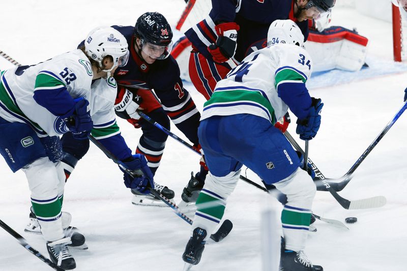 Jan 14, 2025; Winnipeg, Manitoba, CAN;  Vancouver Canucks forward Phillip Di Giuseppe (34), Vancouver Canucks forward Teddy Blueger (53) and Winnipeg Jets defenseman Ville Heinola (14) contest for the puck for puck  during the third period at Canada Life Centre. Mandatory Credit: Terrence Lee-Imagn Images