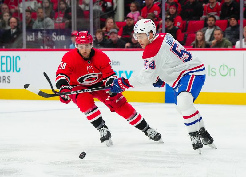 Dec 28, 2023; Raleigh, North Carolina, USA; Montreal Canadiens defenseman Jordan Harris (54) tires to control the puck against Carolina Hurricanes left wing Michael Bunting (58) during the first period at PNC Arena. Mandatory Credit: James Guillory-USA TODAY Sports