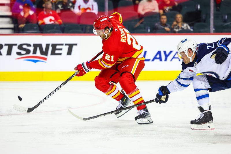 Oct 4, 2024; Calgary, Alberta, CAN; Calgary Flames center Kevin Rooney (21) controls the puck in front of Winnipeg Jets left wing Nikolaj Ehlers (27) during the second period at Scotiabank Saddledome. Mandatory Credit: Sergei Belski-Imagn Images