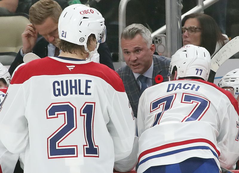 Nov 2, 2024; Pittsburgh, Pennsylvania, USA;  Montreal Canadiens head coach Martin St. Louis (rear) talks to defenseman Kaiden Guhle (21) and center Kirby Dach (77) on the bench against the Pittsburgh Penguins during the third period at PPG Paints Arena. Mandatory Credit: Charles LeClaire-Imagn Images