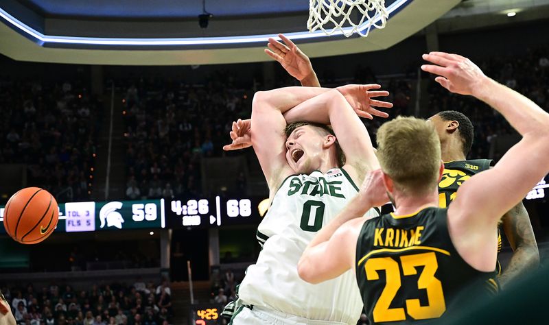 Feb 20, 2024; East Lansing, Michigan, USA;  Michigan State Spartans forward Jaxon Kohler (0) gets fouled under the basket by Iowa Hawkeyes guard Tony Perkins (11) and forward Ben Krikke (23) during the second half at Jack Breslin Student Events Center. Mandatory Credit: Dale Young-USA TODAY Sports
