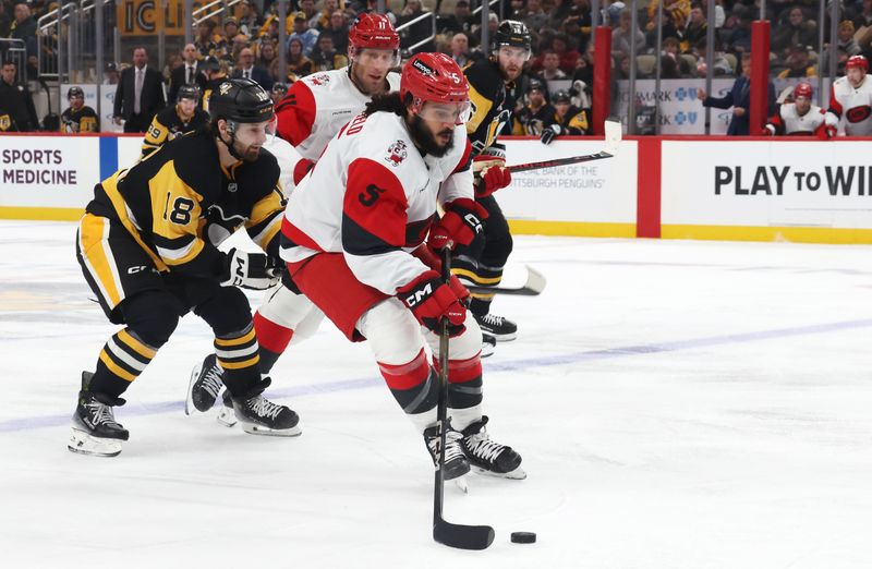Dec 30, 2025; Pittsburgh, Pennsylvania, USA; Carolina Hurricanes defenseman Jalen Chatfield (5) carries the puck into the offensive zone against Pittsburgh Penguins center Tommy Novak (18) during the second period at PPG Paints Arena. Mandatory Credit: Charles LeClaire-Imagn Images