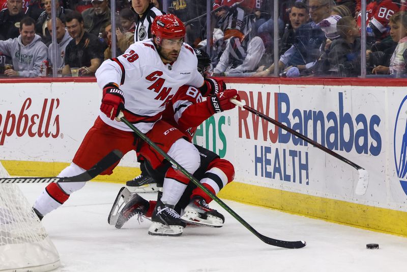 Nov 21, 2024; Newark, New Jersey, USA; Carolina Hurricanes left wing William Carrier (28) and New Jersey Devils center Jack Hughes (86) battle for the puck during the third period at Prudential Center. Mandatory Credit: Ed Mulholland-Imagn Images