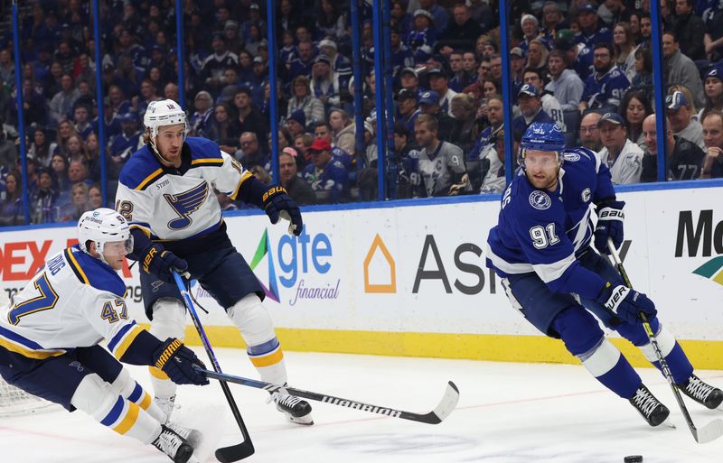 Dec 19, 2023; Tampa, Florida, USA; Tampa Bay Lightning center Steven Stamkos (91) skates with the puck as St. Louis Blues defenseman Torey Krug (47) and right wing Kevin Hayes (12) defend during the first period at Amalie Arena. Mandatory Credit: Kim Klement Neitzel-USA TODAY Sports