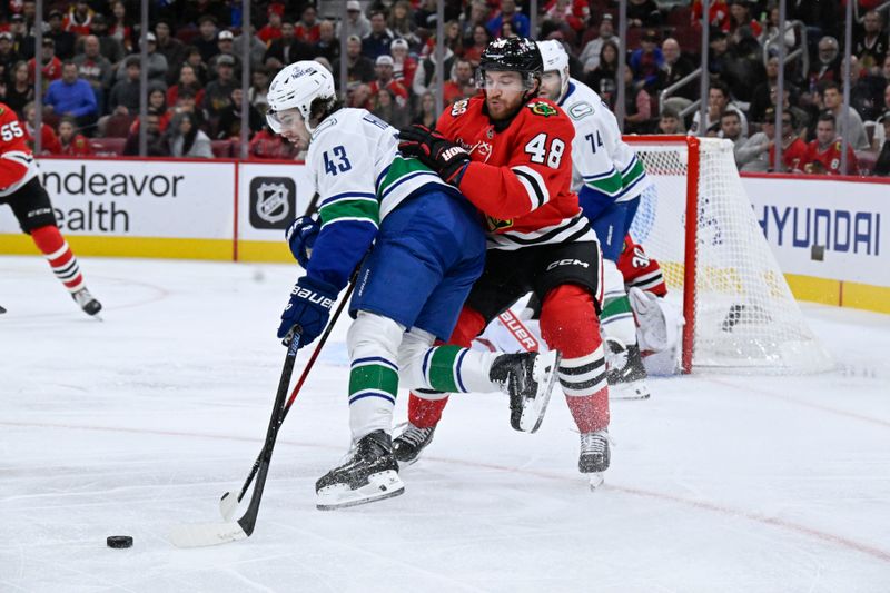 Oct 17, 2025; Chicago, Illinois, USA;  Vancouver Canucks defenseman Quinn Hughes (43) and Chicago Blackhawks defenseman Matt Grzelcyk (48) chase the puck during the first period at the United Center. Mandatory Credit: Matt Marton-Imagn Images