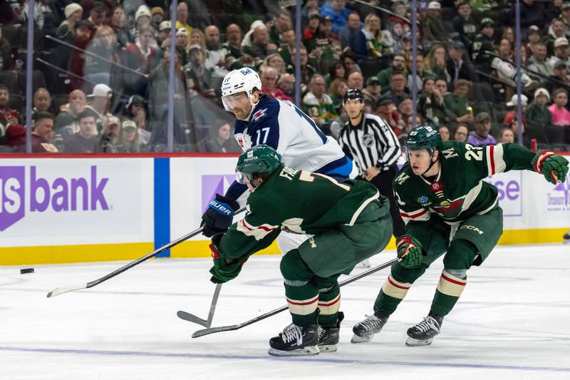 Nov 25, 2024; Saint Paul, Minnesota, USA;  Winnipeg Jets forward Adam Lowry (17) backhands the puck for an empty net goal as Minnesota Wild defenseman Brock Faber (7) and forward Marco Rossi (23) defend during the third period at Xcel Energy Center. Mandatory Credit: Nick Wosika-Imagn Images